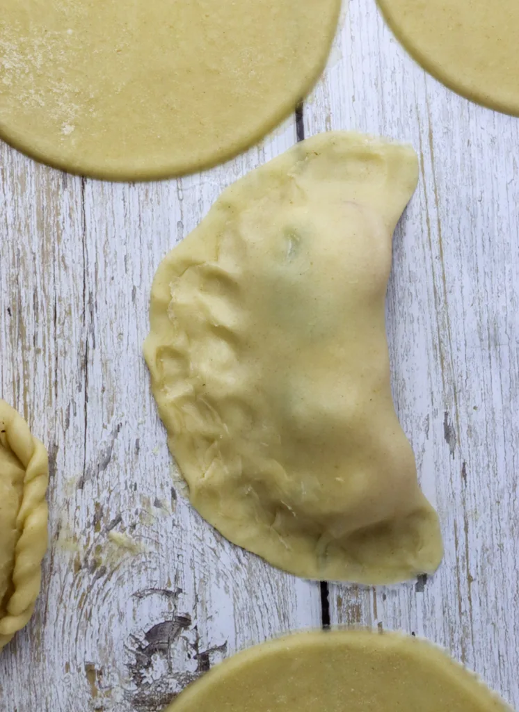step: image showing how to fold over the disc and pressing the edges down using your fingers to assemble the empanadas