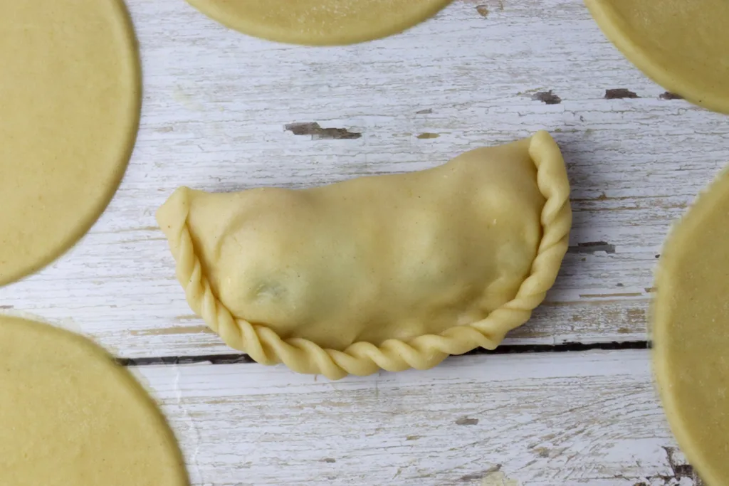 step - how to twist the edges, hold the folded empanada in your hands, and start twisting the edge of the dough to the inside of the empanada, forming a wavy curly pattern from one side to the other