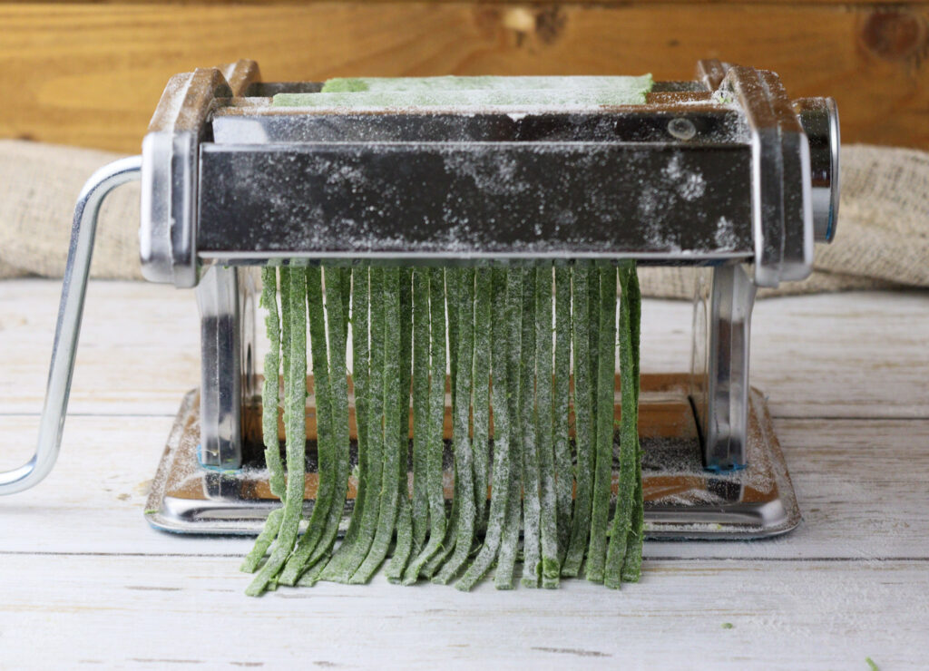 image showing how nice noodles made from green pasta dough are coming out of the pasta maker machine 