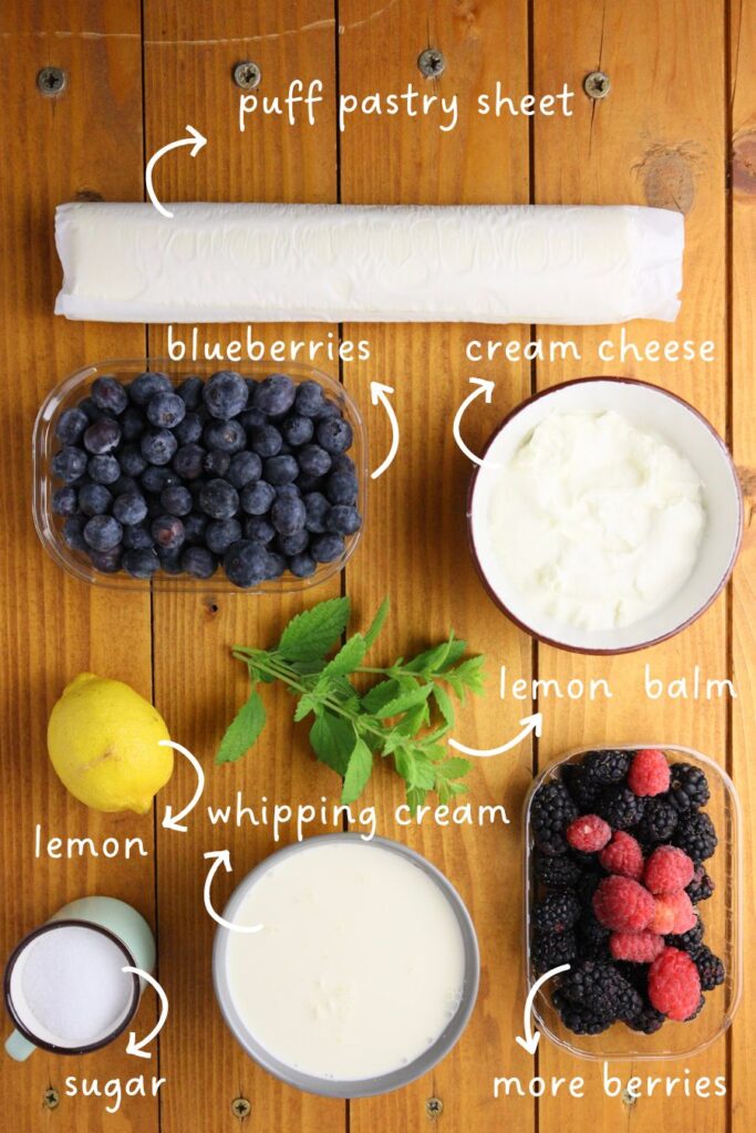 gathering ingredients for fruit tarts with puff pastry: blackberries, blueberries, raspberries, cream cheese, whipping cream, puff pastry sheets, lemon, lemon balm leaves and sugar