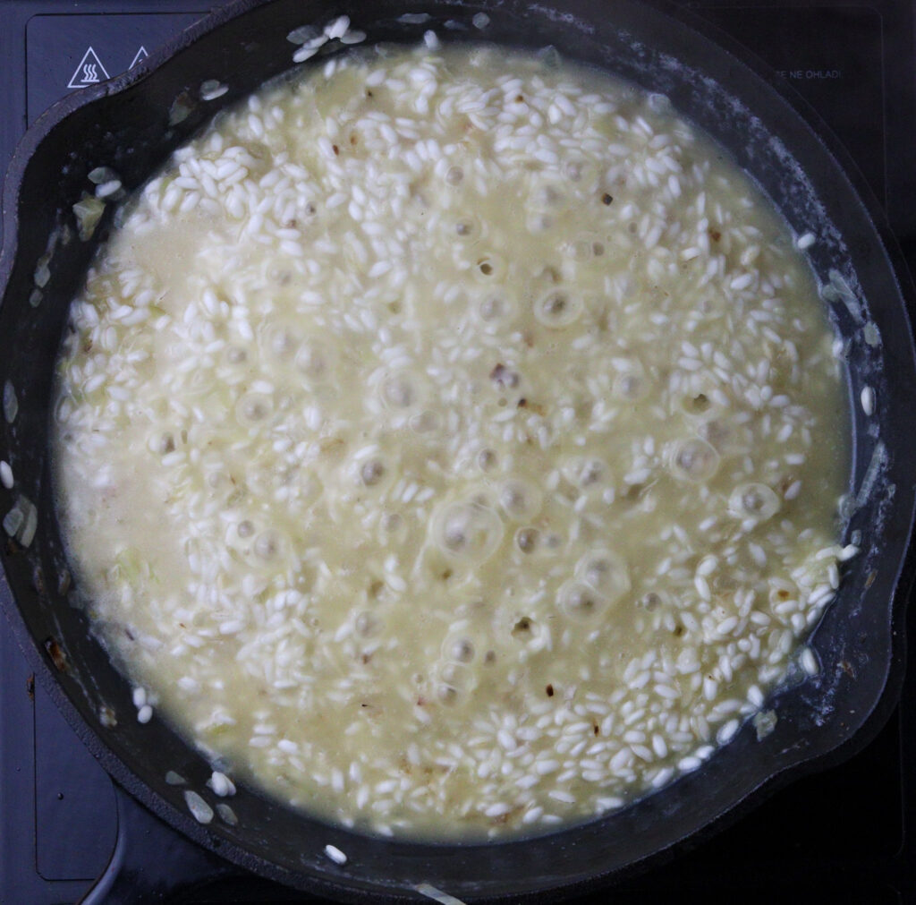 How to keep gradually adding liquid when cooking risotto. Image showig risotto slowly cooking. 
